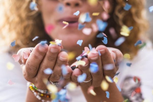 beautiful defocused woman blow confetti from hands. celebration and event concept. happiness and colored image. movement and happiness having fun