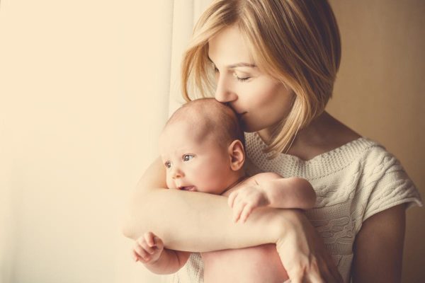 newborn baby in a tender embrace of mother at the window