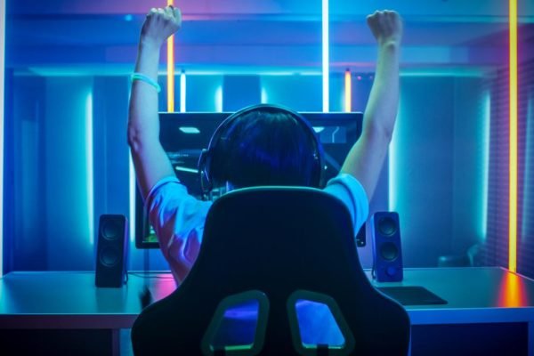 Professional Gamer Playing and Winning in First-Person Shooter Online Video Game on His Personal Computer. Footage Fade out into Bokeh. Room Lit by Neon Lights in Retro Arcade Style. Cyber Sport Championship.