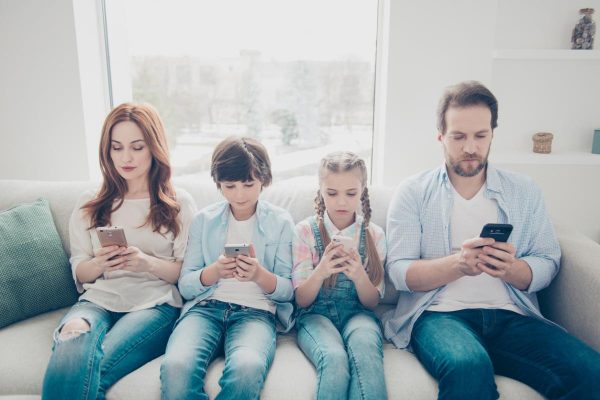 Portrait of family with two kids holding smart phones having electronic devices in hands texting sms using wi-fi 3G internet checking email searching contact. Apps concept
