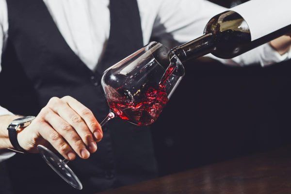 Close up shot of sommelier pouring red wine from bottle in glass
