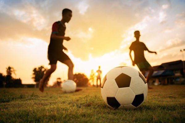 Silhouette action sport outdoors of a group of kids having fun playing soccer football for exercise in community rural area under the twilight sunset sky.