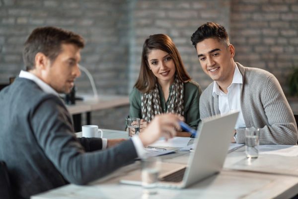 Happy couple using laptop with their insurance agent during a meeting.